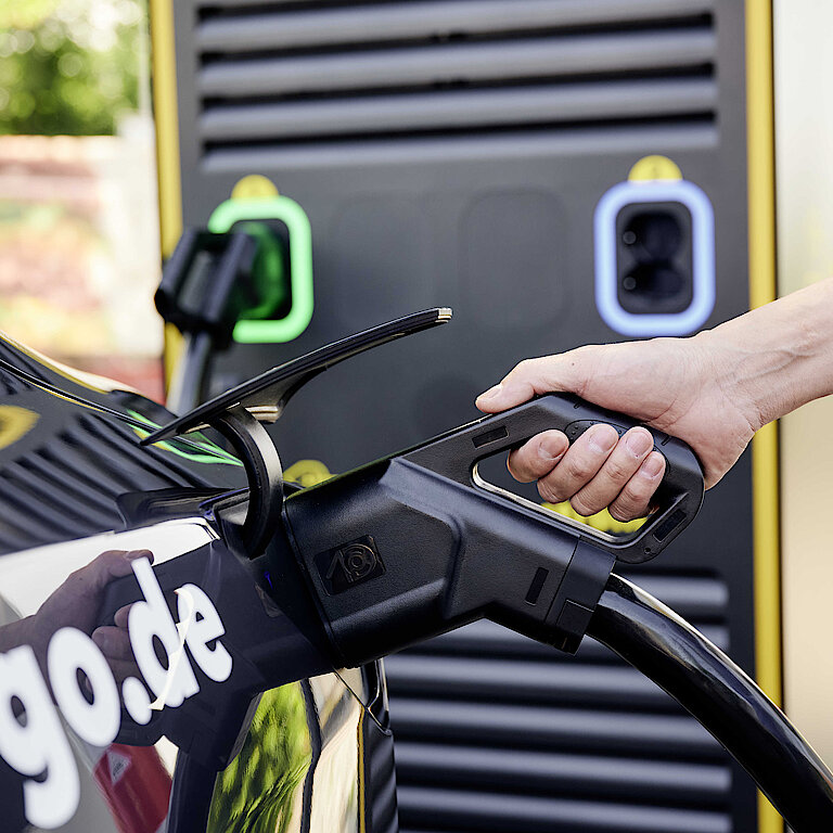 Hand hält eine Zapfpistole für Elektroautos in der Hand, um E-Auto betanken zu lassen.