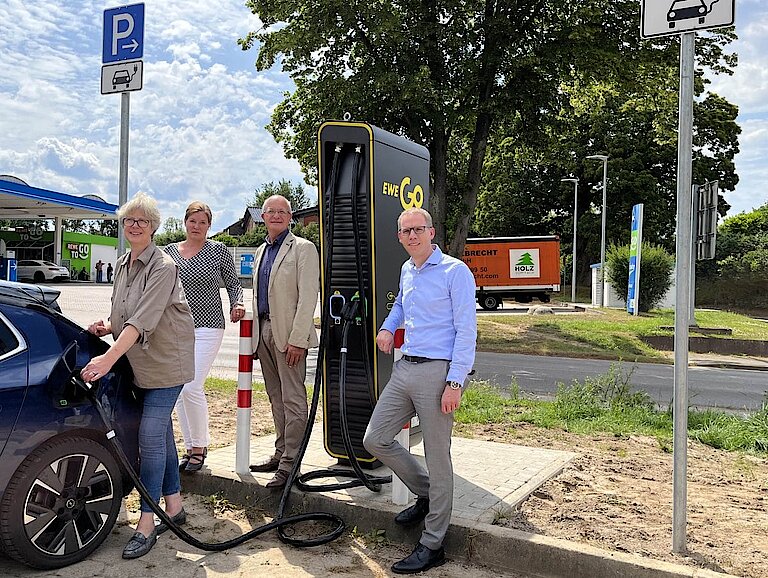 Vier Personen stehen neben einer EWE Go Ladesäule und betanken ein Elektroauto.