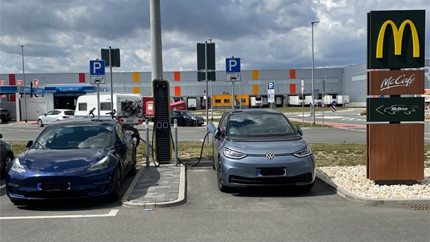 Zwei PKW werden an einer EWE Go Ladesäule vor einem McDonalds-Restaurant aufgeladen.